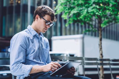 Resmi olarak giyinmiş tüccar, dijital tabletteki 4G internete bağlı finansal web sitesinde para transferi bilgilerini kontrol ediyor. Gözlüklü adam yatırımcılarla göz koruma sohbeti sağlıyor.