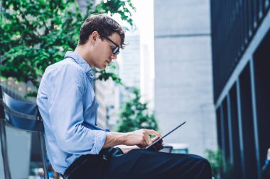 Girişimcinin, kentsel ortamlarda otururken dijital tablette sohbet edişinin yan görüntüsü, şehirde iş arasında elektronik kitap okuyan erkek avukat, uygulama yüklemek için 4G kablosuz ağ kullanıyor