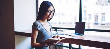 Sosyal ağda yayınlanması için dizüstü bilgisayarla yeni makaleler yazan olumlu içerik yazarı, kafeterya masasının yanında netbook ile otururken sınava hazırlanan mutlu bayan öğrenci