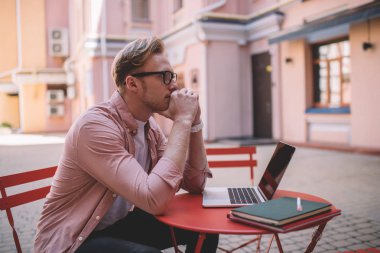 Optik gözlük takan kafası karışmış erkek öğrenci, e-öğrenim için göz koruması sağlıyor ve ders için bilgi hazırlıyor, web sitesi sisteminde düşünceli serbest yazar