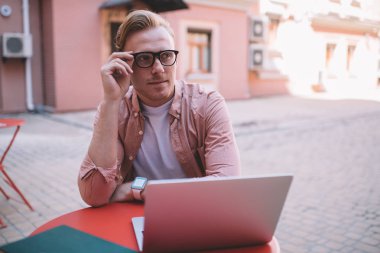 Klasik görüş koruması için gözlüklü, düşünceli hippi bir adam kafeterya masasında oturmuş web sitesi içeriği üzerine kafa yoruyor. Modern dizüstü bilgisayarla uzaktan çalışan dalgın hipster programcı.