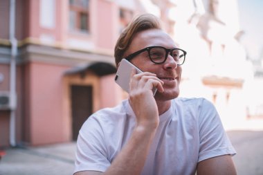Millennial pozitif hipster 'ın arkadaşıyla cep telefonu konuşması iyi haberlerin keyfini çıkarıyor, görme gözlüklü mutlu bir adam akıllı telefon aracılığıyla iletişim kuruyor.