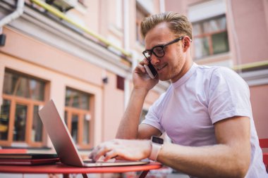Klasik göz giysisi içindeki olumlu beyaz adam cep telefonu uygulaması üzerinden uluslararası gezinti kullanarak resimleri düzenlemek için medya uygulaması danışmanlığı için müşteri hizmetlerine çağrı yapıyor.