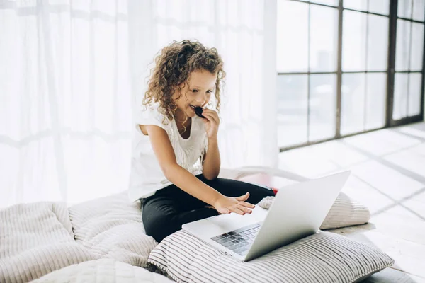 Söt liten flicka med laptop kylning på kuddar — Stockfoto