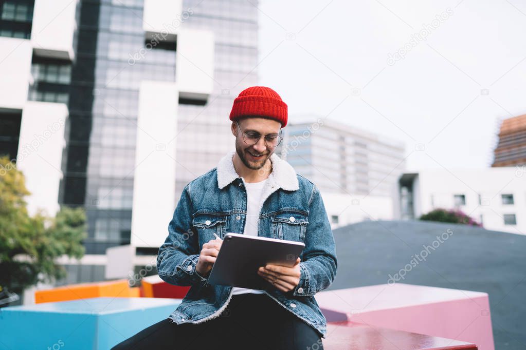 Positive Caucasian male in casual denim jacket and stylish optical spectacles for provide eyes protection enjoying online communication and virtual friendship with followers from social website
