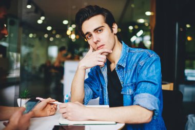 Masada otururken kameraya bakan yakışıklı genç adamın portresi ve modern uzayda birlikte çalışma seminerine hazırlanan bilgileri yazmak. Ödev yapan hippi çocuk.
