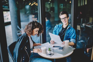 Kafe iç işlerinde kadın ortakla işbirliği yapan olumlu hipster adamın portresi. Yönetim muhasebesi, zeki erkek ve kadın üniversite sınavına hazırlanıyor.