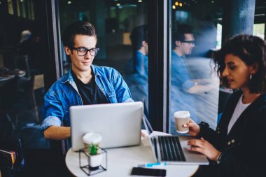 Gündelik giyinmiş iki hippi öğrenci birbirleriyle iletişim kuruyor ve modern dizüstü bilgisayarda çalışmak ve modern uzayda kablosuz internet bağlantısı kullanmak için uygulamaları tartışıyorlar.