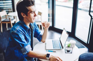 Gündelik giyinmiş, uzaktan kumandalı dizüstü bilgisayarda çalışan uygulama için veritabanını güncelleyen düşünceli genç bir adam. Ders için ayrıntıları düşünen düşünceli bir erkek öğrenci.