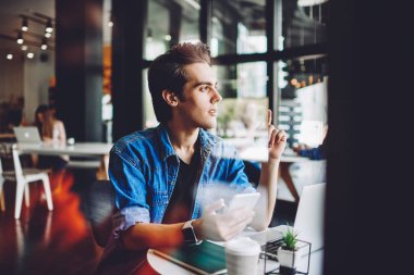 Düşünceli erkek öğrenci haberleşmek için dijital teknolojiler kullanıyor. Arkadaşını tanıtım alanında bekliyor. Düşünceli 20li yaşlardaki hippi çocuk elinde akıllı telefon tutuyor.