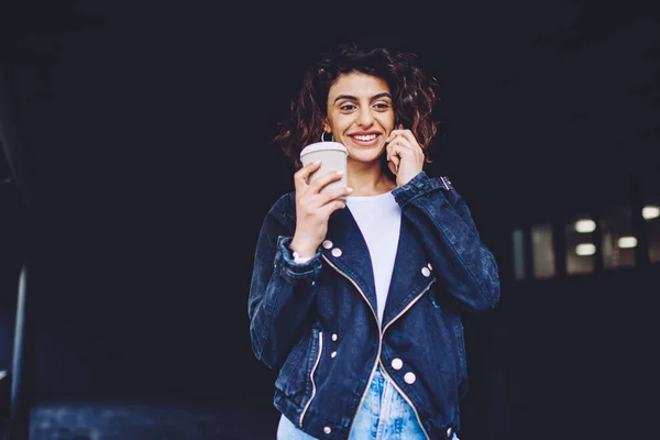 Cheerful female hipster enjoying caffeine beverage and friendly mobile conversation via new application and roaming connection, happy woman feeling good during international call via cellphone
