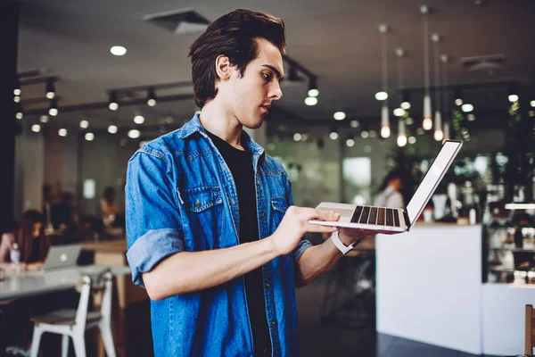 Serious male programmer testing created application on laptop computer during distance job on publicity area, skilled hipster guy searching document file on modern netbook connected to wifi