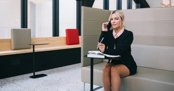 Female proud ceo calling on smartphone to solve financial issues during work with literature, portrait of caucasian attractive businesswoman talking on mobile phone device in office interior