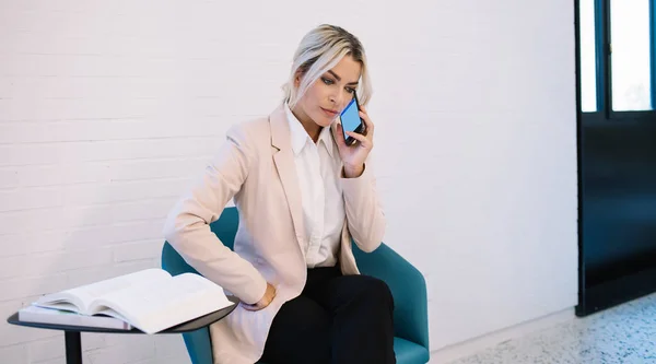 4Gワイヤレスに接続されたビジネス契約を議論するために従業員に電話する深刻なビジネス女性 教科書とテーブルの近くに座っているブロンドの女性弁護士 会話をするための無線Lanを使用して — ストック写真