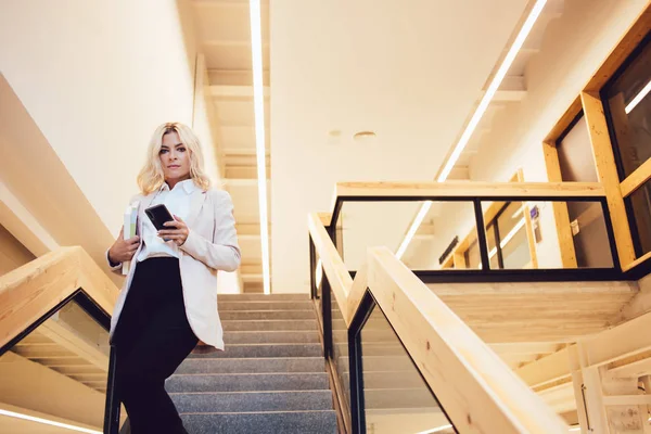 ビジネスミーティングの途中でカメラを見て魅力的な白人女性経済学者の半分の長さの肖像 現代のワークショップで階段で通信するためのデジタル電話を使用してエグゼクティブマネージャー — ストック写真