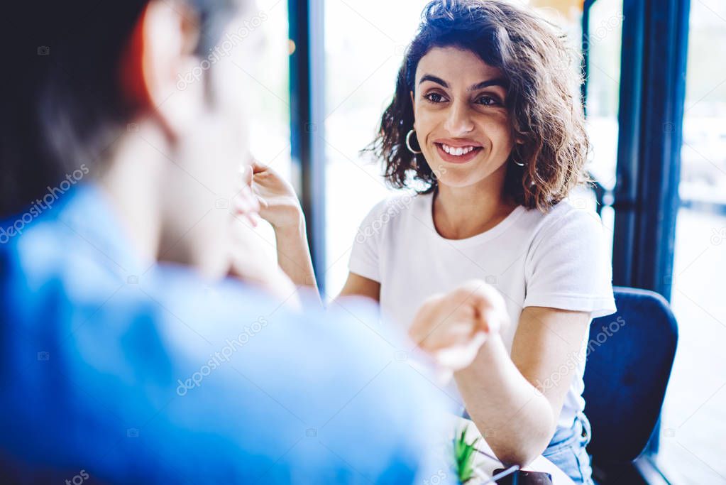 Happy smiling couple enjoying time with each other in comfortable cafeteria, cheerful caucasian woman in casual wear talking interesting story from life to male friend sitting at front and listening