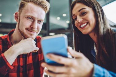 Neşeli erkek ve kadın, cep telefonuyla iletişim kurmak için web kamerası ve uygulama kullanan arkadaşlarıyla olumlu video görüşmesinden keyif alıyor, mutlu hipsterler cep telefonuyla sosyal ağdan komik haberler okuyor.
