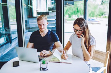 Konsantre kadın organizatör müşterileri arama planı hakkında tartışmak için ana notlar yazmak için akıllı telefon cihazında 4g internet kullanarak erkek arkadaş netbook üzerinden sohbet ederken