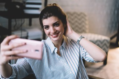 Mutlu kadın blogcu, yeni takipçileri çekmek için kendi web sayfasında kendi fotoğrafını çekiyor. Yüzünde sevimli bir gülümseme olan pozitif hipster kız ön kamerayla fotoğraf çekiyor.