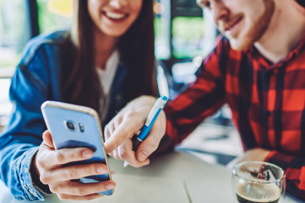 Обрезанное изображение студентов мужского и женского пола, просматривающих социальные сети через сотовый телефон во время перерыва от учебы в помещении, друзей, ищущих информацию на веб-сайте через гаджет смартфона