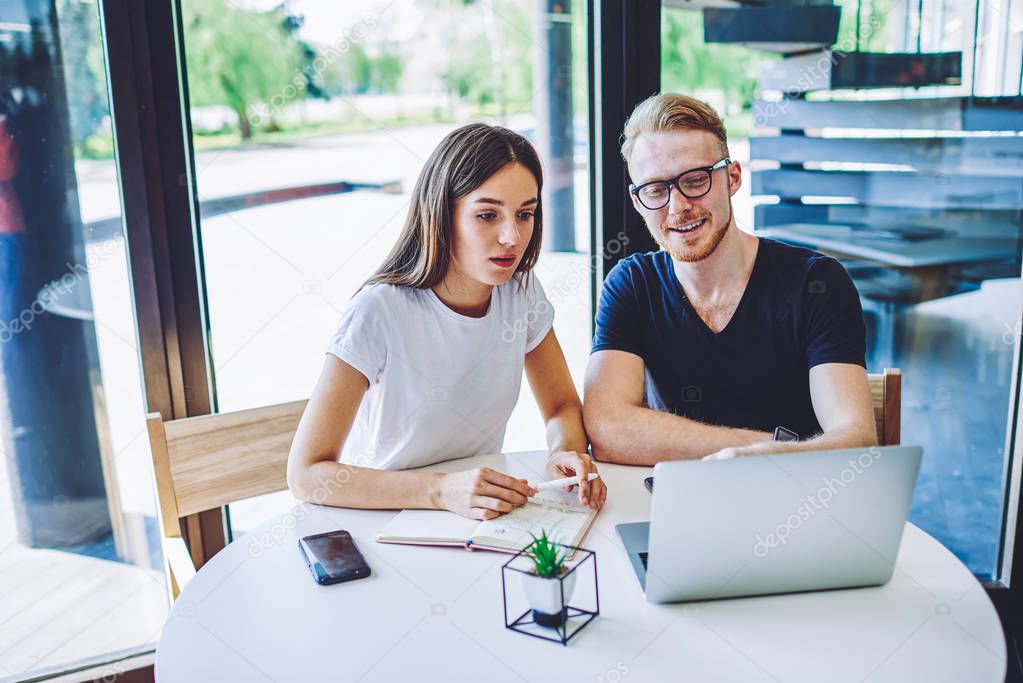 Young male and female freelancers searching interesting information for creating content article for web store using free wireless connection on new laptop device and textbook for making notes