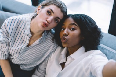 Çekici afro-amerikan ve beyaz kadın arkadaşlarının yakın portresi ördek suratı yapıyor ve birlikte vakit geçirirken kameraya bakıyor evde boş zaman geçiriyor, çok kültürlü insanlar.