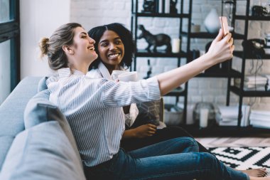 Kahve saatinde akıllı telefondan fotoğraf çeken mutlu iki bayan arkadaş. Afro beyaz model ve Afro-Amerikan hipster kız. Blog 'da yayınlamak için telefonla fotoğraf çekiyor.