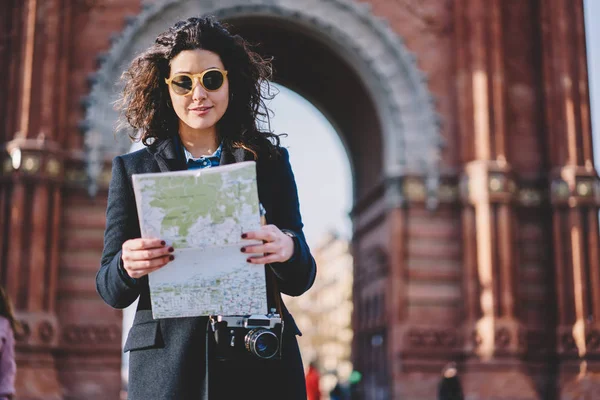 Günlük kıyafetleri ve güneş gözlükleriyle gezen genç beyaz tenli gezgin, kağıt haritada ünlü caddenin yerini araştırıyor, şehrin etrafını gezmek için klasik kamera okuma güzergahı olan çekici bir kadın.