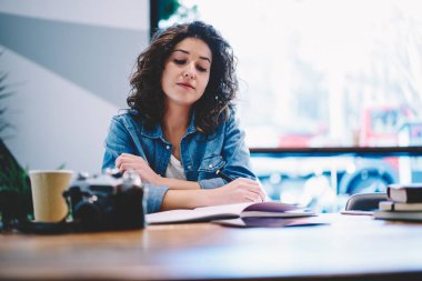 Gündelik giyinmiş ciddi bir kız öğrenci kafenin içinde öğrenim görmek için zaman geçirdiği sırada bilgi kitaplarından gelen bilgileri analiz etmekten yorgun düşmüş ve evde notlar okuyan bir kadın.