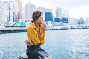Hong Kong 'un arka planında dinlenirken, tatil boyunca kafa yoran Japon bir kadının dinlenme yerlerinde keyif çattığı yemek fincanından nefis kafein içen dalgın bir bayan turist.