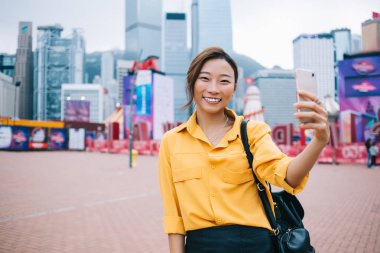 Çin tatillerinde web bloguna paylaşmak için selfie çekilen pozitiflerin yarım boy portresi, kameraya gülümseyen ve kendini fotoğraflayan komik hippi kız.