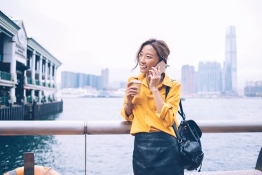 Başarılı hipster kızı, Hong Kong 'da Çin tatili için en iyi arkadaşına telefon ediyor. Neşeli kadın, Victoria Körfezi yakınlarındaki kahve saatinde cep telefonu sohbetinden hoşlanıyor.