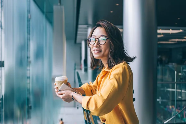 公共の場所で自由な時間の間にカメラで微笑む古典的なメガネで陽気なヒップスターの女の子の半分の長さの肖像画 肯定的な中国の女性ブロガーは インターネットサーフィンのためのスマートフォンデバイスを保持 — ストック写真