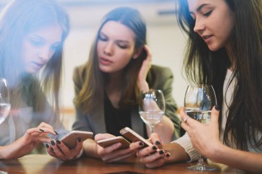 Beyaz çağdaki kadınların internette sosyalleşmesi ve arkadaşlarıyla şarap saatinde canlı iletişimi yok sayması. Modern cep telefonlarıyla sohbet eden güzel hipster kızları.