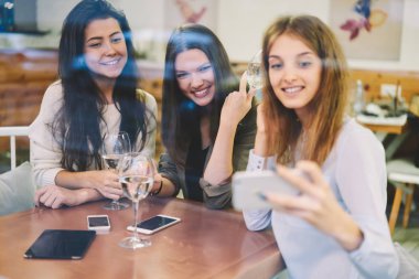 Kafeteryada boş zamanlarında selfie için poz veren pozitif kadın blogcular, arkadaşlarıyla evde otururken modern cep telefonunda fotoğraf çeken mutlu bir kadın.