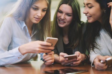 Kendi seyahat blogunda takipçilerle çevrimiçi mesajlaşmak için cep telefonlarında ücretsiz internet bağlantısı kullanarak yayınlama altında komik yorumlar okuyan gündelik görünümlü olumlu gülümseyen kadınlar