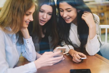 Mutlu gülümseyen kadın blogcular, akıllı telefon zımbırtısıyla ücretsiz internete bağlı sosyal ağda yayın yapmak için arkadaşa olumlu mesaj okuyor, neşeli kadınlar video izliyor.