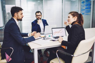 Çalışan iş adamları toplantı odasında modern bilgisayarlarla birlikte oturuyorlar, akıllı işçiler şirketin yeni strateji gelişimini analiz ediyor ve tartışıyorlar netbook 'taki grafikleri kullanarak.