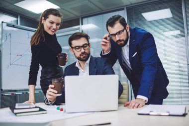 Mutlu resmi iş ekibi kahve içiyor ve internet üzerinden sohbet etmek için iş yerinde dinleniyor. Gözlüklü adam, meslektaşlarına son sunumlarının videosunu modern laptopta gösteriyor.