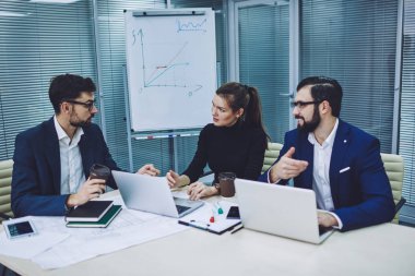 Kendine güvenen erkek ve kadın tüccarlar modern şirket ofisinde işbirliği içinde vakit geçiriyorlar. Beyaz iş adamları resmi olarak iş yerinde verimli bir konferans için fikir alışverişinde bulunuyorlar.