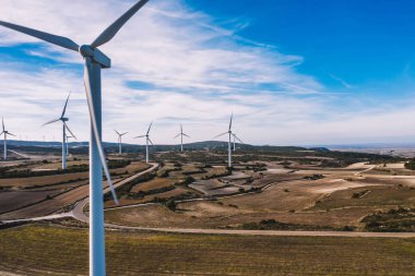 Kırsal tarım ortamında eko kaynaklarından alternatif temiz yeşil enerji üreten dönen pervaneli yel değirmenlerinin hava görüntüsü. Kuş bakışı türbinlerin elektrik üreten hattına bakıyor.