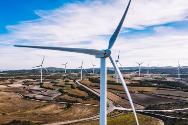 Kırsal tarım ortamında eko kaynaklarından alternatif temiz yeşil enerji üreten dönen pervaneli yel değirmenlerinin hava görüntüsü. Kuş bakışı türbinlerin elektrik üreten hattına bakıyor.
