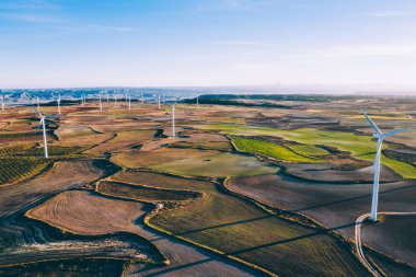 Kırsal tarım ortamında eko kaynaklarından alternatif temiz yeşil enerji üreten dönen pervaneli yel değirmenlerinin hava görüntüsü. Kuş bakışı türbinlerin elektrik üreten hattına bakıyor.