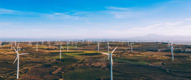 Kırsal tarım ortamında eko kaynaklarından alternatif temiz yeşil enerji üreten dönen pervaneli yel değirmenlerinin hava görüntüsü. Kuş bakışı türbinlerin elektrik üreten hattına bakıyor.