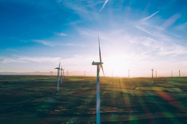 Turuncu günbatımı gökyüzü üzerinde kırsal tarım arazisi tarım çayırında duran dönen pervaneler ile modern yel değirmenleri. Temiz kaynaklar için yenilenebilir enerji üreten rüzgar üfleme. Elektrik enerjisi üretimi
