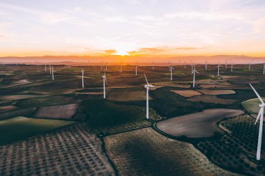 Turuncu günbatımı gökyüzü üzerinde kırsal tarım arazisi tarım çayırında duran dönen pervaneler ile modern yel değirmenleri. Temiz kaynaklar için yenilenebilir enerji üreten rüzgar üfleme. Elektrik enerjisi üretimi