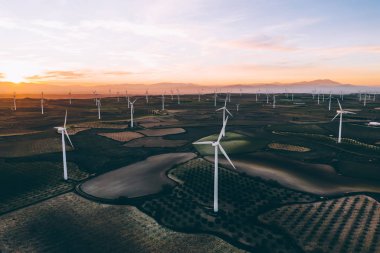 Turuncu günbatımı gökyüzü üzerinde kırsal tarım arazisi tarım çayırında duran dönen pervaneler ile modern yel değirmenleri. Temiz kaynaklar için yenilenebilir enerji üreten rüzgar üfleme. Elektrik enerjisi üretimi
