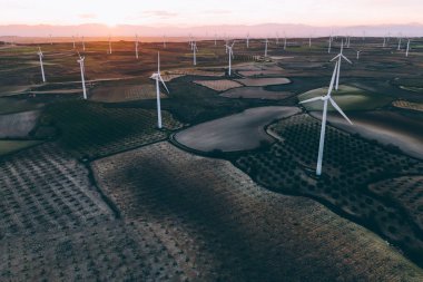 Turuncu günbatımı gökyüzü üzerinde kırsal tarım arazisi tarım çayırında duran dönen pervaneler ile modern yel değirmenleri. Temiz kaynaklar için yenilenebilir enerji üreten rüzgar üfleme. Elektrik enerjisi üretimi