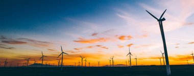 Mavi günbatımı gökyüzüne karşı kırsal tarım ortamında Eko kaynaklardan alternatif temiz yeşil güç üreten pervaneler ile yel değirmenleri İstasyonu silueti. Elektrik üreten türbinlerin çiftliği