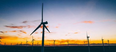 Mavi günbatımı gökyüzüne karşı kırsal tarım ortamında Eko kaynaklardan alternatif temiz yeşil güç üreten pervaneler ile yel değirmenleri İstasyonu silueti. Elektrik üreten türbinlerin çiftliği